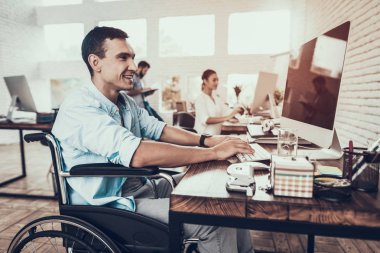 Tekerlekli sandalye ofiste bilgisayar üzerinde çalışan adam. Genç adam adam tekerlekli sandalye üzerinde devre dışı. Kurtarma ve sağlık kavramları. Office çalışmasında. Genç bir işçi. Oturan adam adam bilgisayar ile.