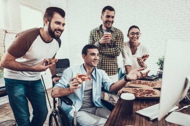 Gençler Pizza ile ofiste yemek. Office çalışmasında. Genç bir işçi. Oturan adam Pizza kutusu. Genç kız bardaklarda. Genç bir işçi. Molada Yöneticisi. Adam tekerlekli sandalye üzerinde.