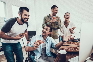 Gençler Pizza ile ofiste yemek. Office çalışmasında. Genç bir işçi. Oturan adam Pizza kutusu. Genç kız bardaklarda. Genç bir işçi. Molada Yöneticisi. Adam tekerlekli sandalye üzerinde.
