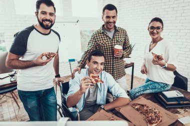 Gençler Pizza ile ofiste yemek. Office çalışmasında. Genç bir işçi. Oturan adam Pizza kutusu. Genç kız bardaklarda. Genç bir işçi. Molada Yöneticisi. Adam tekerlekli sandalye üzerinde.