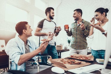 Gençler Pizza ile ofiste yemek. Office çalışmasında. Genç bir işçi. Oturan adam Pizza kutusu. Genç kız bardaklarda. Genç bir işçi. Molada Yöneticisi. Adam tekerlekli sandalye üzerinde.
