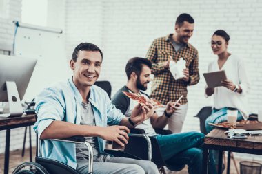 Gençler Pizza ile ofiste yemek. Office çalışmasında. Genç bir işçi. Oturan adam Pizza kutusu. Genç kız bardaklarda. Genç bir işçi. Molada Yöneticisi. Adam tekerlekli sandalye üzerinde.