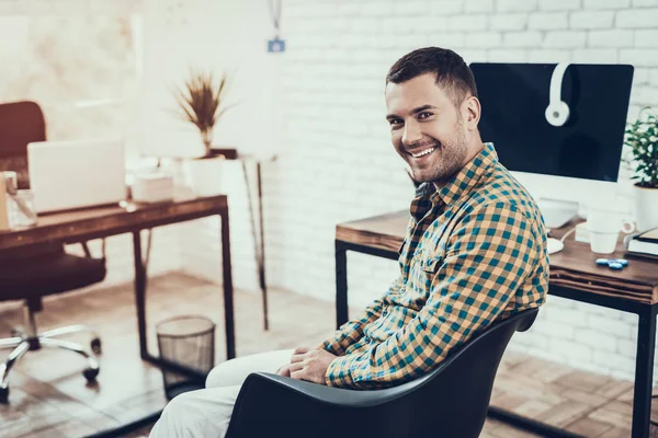 笑顔の若い男が事務所の椅子に座っている 机の上のデジタルデバイス 近代的なオフィス 黒の椅子 髭のない男 オフィスコンセプトで働く 若い労働者 ホワイトルームの男 ホワイト ガジェット — ストック写真