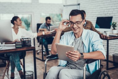 Ofiste Tablet Pc ile tekerlekli sandalye üzerinde gözlüklü adam. Genç adam adam tekerlekli sandalye üzerinde devre dışı. Kurtarma ve sağlık kavramları. Office çalışmasında. Genç bir işçi. Oturan adam işçi gözlük.