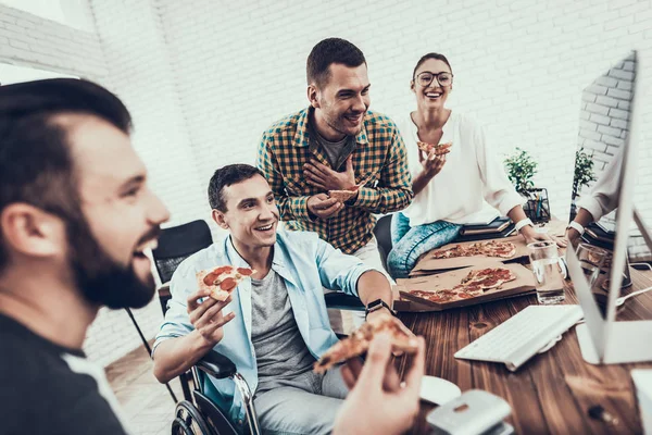 Young People Have Lunch with Pizza in Office. Teamwork in Office. Young Worker. Sitting Man. Box with Pizza. Young Girl in Glasses. Young Worker. Manager on Break. Man on Wheelchair.
