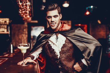 Partide Vampir kostümlü genç adamın portresi. Cadılar Bayramı kostümü giyen yakışıklı bir adam gece kulübünde barın yanında dikiliyor ve korkunç bir yüz ifadesi takınıyor. Cadılar Bayramı Kutlaması