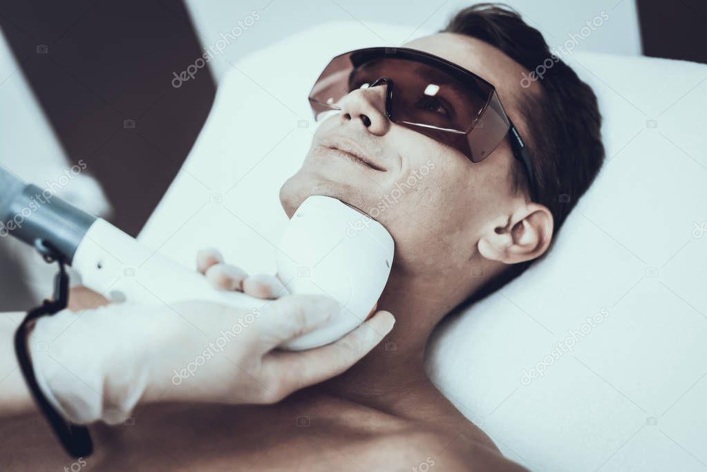 Young Man in Spa Salon for Laser Hair Removal. Guy in Beauty Salon. Modern Cosmetology. Proffesional Cosmetologist. Doctor with Laser Epilator. Men's Beauty Concept. Man in Glasses.