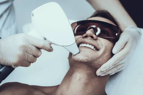 Young Man in Spa Salon for Laser Hair Removal. Guy in Beauty Salon. Modern Cosmetology. Proffesional Cosmetologist. Doctor with Laser Epilator. Men\'s Beauty Concept. Medical Equipment.