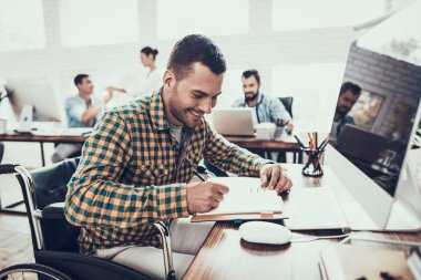 Tekerlekli sandalyedeki genç adam not defterine not tutuyor. Oturan Adam. Not defterine yazıyorum. Engelli genç adam. Tekerlekli sandalyedeki adam. İyileşme ve Sağlık Hizmetleri Konsepti. Ofiste takım çalışması. Genç İşçi.