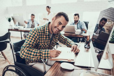 Tekerlekli sandalyedeki genç adam not defterine not tutuyor. Oturan Adam. Not defterine yazıyorum. Engelli genç adam. Tekerlekli sandalyedeki adam. İyileşme ve Sağlık Hizmetleri Konsepti. Ofiste takım çalışması. Genç İşçi.
