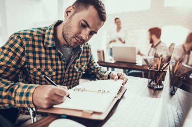 Tekerlekli sandalyedeki genç adam not defterine not tutuyor. Oturan Adam. Not defterine yazıyorum. Engelli genç adam. Tekerlekli sandalyedeki adam. İyileşme ve Sağlık Hizmetleri Konsepti. Ofiste takım çalışması. Genç İşçi.