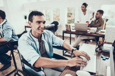 Tekerlekli sandalye ofiste bilgisayar üzerinde çalışan adam. Genç adam adam tekerlekli sandalye üzerinde devre dışı. Kurtarma ve sağlık kavramları. Office çalışmasında. Genç bir işçi. Oturan adam adam bilgisayar ile.