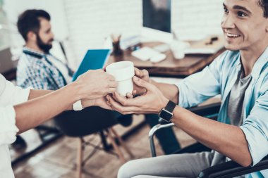 Adam tekerlekli sandalyede Office Kupası veren kadın. Genç adam adam tekerlekli sandalye üzerinde devre dışı. Kurtarma ve sağlık kavramları. Office çalışmasında. Genç bir işçi. Adam telefonda konuşurken oturan.