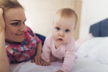 Şirin mavi gözlü bebek kaynıyor anne yatakta yakınındaki. Neşeli beyaz yalan ve güzel güzel çocuk kapalı seyir annesi gülümseyerek. Mutlu annelik ve çocukluk kavramı