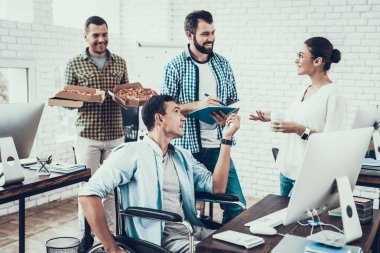 Gençler Pizza ile ofiste yemek. Office çalışmasında. Genç bir işçi. Oturan adam Pizza kutusu. Genç kız bardaklarda. Genç bir işçi. Molada Yöneticisi. Adam tekerlekli sandalye üzerinde.