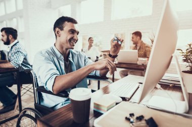 Tekerlekli sandalye ofiste bilgisayar üzerinde çalışan adam. Genç adam adam tekerlekli sandalye üzerinde devre dışı. Kurtarma ve sağlık kavramları. Office çalışmasında. Genç bir işçi. Oturan adam adam bilgisayar ile.