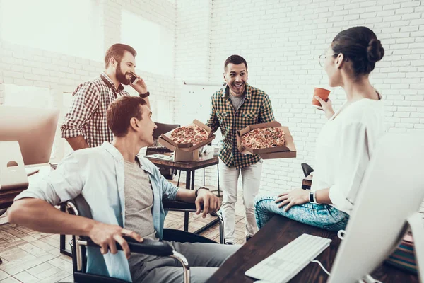 Gençler Pizza ile ofiste yemek. Office çalışmasında. Genç bir işçi. Oturan adam Pizza kutusu. Genç kız bardaklarda. Genç bir işçi. Molada Yöneticisi. Adam tekerlekli sandalye üzerinde.