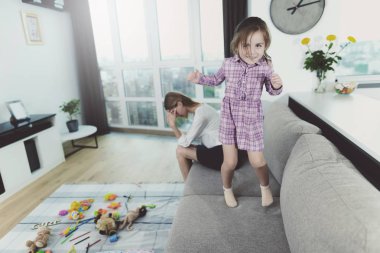 Kız sahip eğlenceli atlama Divan Anne ne zaman üzgün. Parlak Modern oturma odasında büyük rahat kanepede karışıklık çevrede çocuk. Anne hayal kırıklığına Holding başkanı geliyor