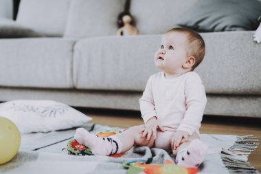 Oturma odasında halı üzerinde oynayan sevimli çocuk. Tatlı şirin güzel beyaz bebek oturan yalnız kanepe yakınındaki halıda oyuncaklarla portresi. Beyaz elbise giyen küçük kız. Çocukluk kavramı
