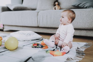 Oturma odasında halı üzerinde oynayan sevimli çocuk. Tatlı şirin güzel beyaz bebek oturan yalnız kanepe yakınındaki halıda oyuncaklarla portresi. Beyaz elbise giyen küçük kız. Çocukluk kavramı