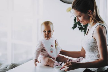 Evde mutlu gülümseyen anne beslemeleri çok güzel evlat. Bright salon şirin aç yürümeye başlayan çocuk sahip odaya kase annelik ve çocukluk kavramı yakınındaki masada otururken anne ile