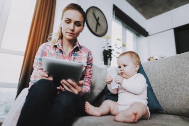Genç Anne ve şirin çocuk telefon ve Tablet kullanır. Mutlu portre? aucasian çok güzel çocuk ile oturma odasında kanepede oturan anne. Ebeveynlik ve çocukluk kavramı
