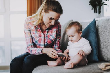 Genç Anne ve şirin çocuk Smartphone kullanarak. Mutlu portre? aucasian annesi oturma sevimli çocuk yatak odası panoramik penceresinde yakınındaki kanepede. Ebeveynlik ve çocukluk kavramı