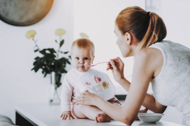 Mutlu anne bebek kaşık ile kapalı besleme. Bright salon şirin aç yürümeye başlayan çocuk sahip odaya masada otururken annesi ile. Annelik ve çocukluk kavramı