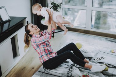 Mutlu genç anne atar Up sevimli çocuk kapalı. Anne giyer Casual giyim çalış tatlı güzel Beyaz Toddler oturur yakınındaki panoramik pencere içinde Modern oturma odası katta ile gülümseyen.