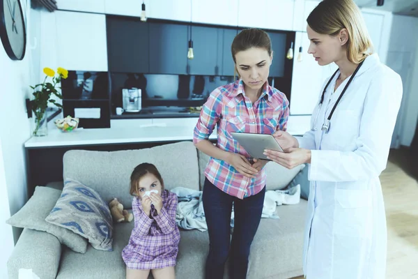 女医生向母亲展示女儿的诊断 白人医疗之光的年轻护士与母亲一起 生病的孩子坐在沙发上的客厅在家里 儿童保健概念 — 图库照片