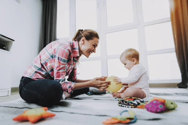 年轻的母亲玩玩具与可爱的婴儿在地毯上 微笑的妈妈穿休闲服装休息与甜蜜的美丽的高加索幼儿附近的大全景窗口在客厅 童年的概念 — 图库照片