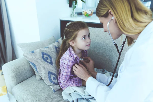 女医生检查生病的孩子在家里 漂亮的小生病的女孩冷坐在沙发上与护士在白色医疗服使用听诊器 儿童健康和医疗保健概念 — 图库照片
