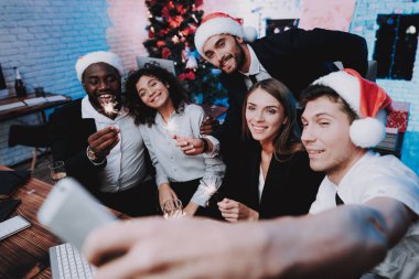 Modern ofis kutluyor yeni yılda gençler. Ofiste Noel ağacı. Bilgisayar masasında. İnsanlar iyi eğlenceler. Kapalı parti. Yeni yıl kutlama. Kırmızı bere genç adam. Noel Baba.