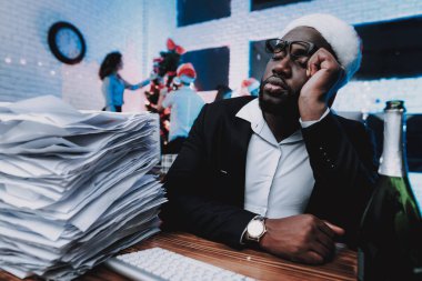 Yeni yıl arifesinde çalışma Office şapkalı yorgun bir adam. Ofiste Noel ağacı. Çalışma iş adamı. Yeni yıl kutlama. Santa Claus şapkalı adam. Belgelerle çalışma. İşadamı gözlük.