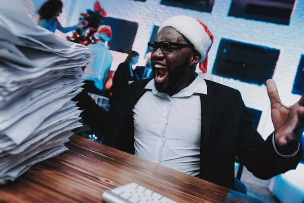 Tired Man in Cap Working in Office on New Year Eve. Christmas Tree in Office. Working Businessman. Celebrating of New Year. Man in Santa Claus Cap. Working with Documents. Businessman in Glasses.