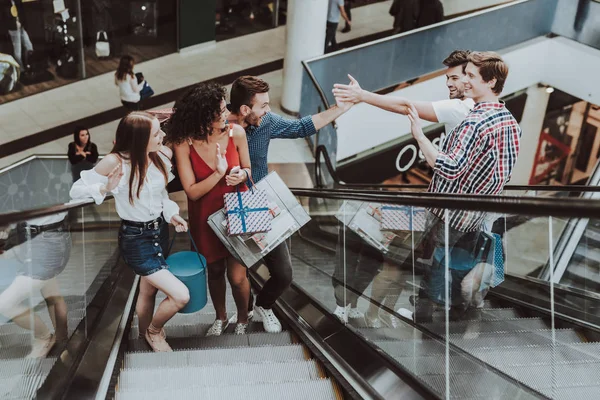 Friends Met on Escalator in Mall on Shopping. Shopping Concept. Girl in Red Dress. Unshaved Young Man. Holding Packages. Pack from Mall in Hands. Greeting to Friends. Escalator in Modern Market.