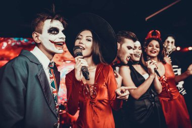 Cadılar Bayramı kostümleri Karaoke şarkı genç insanlar. Mutlu gülümseyerek arkadaşlar giyen eğleniyor şarkı mikrofon ile tarafından gece kulübünde Cadılar Bayramı partisinde kostümleri. Cadılar Bayramı kutlamaları