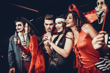 Cadılar Bayramı kostümleri Karaoke şarkı genç insanlar. Mutlu gülümseyerek arkadaşlar giyen eğleniyor şarkı mikrofon ile tarafından gece kulübünde Cadılar Bayramı partisinde kostümleri. Cadılar Bayramı kutlamaları