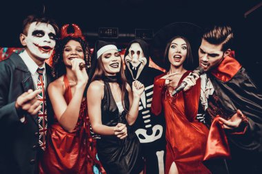 Cadılar Bayramı kostümleri Karaoke şarkı genç insanlar. Mutlu gülümseyerek arkadaşlar giyen eğleniyor şarkı mikrofon ile tarafından gece kulübünde Cadılar Bayramı partisinde kostümleri. Cadılar Bayramı kutlamaları