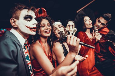 Cadılar Bayramı kostümleri Karaoke şarkı genç insanlar. Mutlu gülümseyerek arkadaşlar giyen eğleniyor şarkı mikrofon ile tarafından gece kulübünde Cadılar Bayramı partisinde kostümleri. Cadılar Bayramı kutlamaları