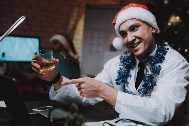 Colleageu fave eğlenceli ofis ile genç doktor. Yeni yıl arifesi. Ofiste Noel ağacı. Bilgisayar masasında. Beyaz ceketli adam. Yeni yıl kutlama. Dijital aygıt kullanarak. Santa Claus Cap.