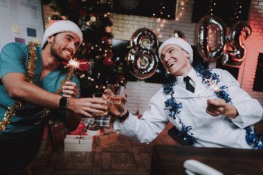 Colleageu fave eğlenceli ofis ile genç doktor. Yeni yıl arifesi. Ofiste Noel ağacı. Bilgisayar masasında. Beyaz ceketli adam. Yeni yıl kutlama. Dijital aygıt kullanarak. Santa Claus Cap.