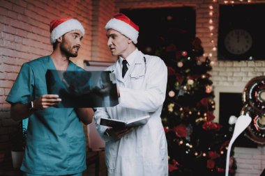 X-ışını ile kırmızı kapaklar iki doktor ofisinde inceden inceye gözden geçirmek. Yeni yıl arifesi. Ofiste Noel ağacı. Bilgisayar masasında. Üniformalı erkeklere. Yeni yıl kutlama. Santa Claus Cap. Tıbbi anlaşmazlık.