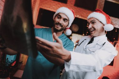 X-ışını ile kırmızı kapaklar iki doktor ofisinde inceden inceye gözden geçirmek. Yeni yıl arifesi. Ofiste Noel ağacı. Bilgisayar masasında. Üniformalı erkeklere. Yeni yıl kutlama. Santa Claus Cap. Tıbbi anlaşmazlık.