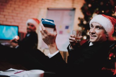 Yeni yıl arifesinde ofiste kırmızı şapkalı işadamları. Hediye kutusu. Ofiste Noel ağacı. Laptop üstünde okul sırası. İş kavramı. Siyah elbiseli adam. Yeni yıl kutlama. Santa Claus Cap.