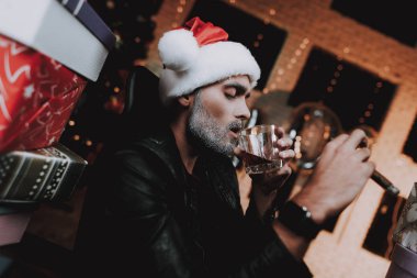 Santa Claus kapaklı hediye kutuları genç adam. Yeni yıl arifesi. Ofiste Noel ağacı. Yeni yıl kutlama. Puro olan adam. Kırmızı şapkalı adam. Kutuları yığını. Alkol İçme oturan adam..