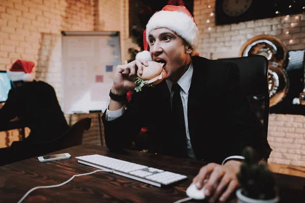 生意人玩电脑和吃汉堡 在办公室的圣诞树 书桌上的笔记本电脑 业务理念 穿黑色西装的男人庆祝新年 使用数字设备 — 图库照片