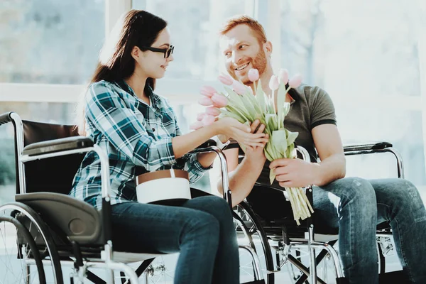 Person in Wheelchair. Woman Disabled with Flowers. Panoramic View. White Interior. Romantic Meeting Disabled. Loving Disabled. People with Limited Opportunities. White Gift Box. White Box and Flowers.