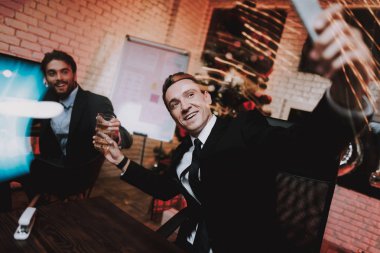 Yeni yıl arifesinde Smartphone kullanarak iş adamı. Ofiste Noel ağacı. Laptop üstünde okul sırası. İş kavramı. Siyah elbiseli adam. Yeni yıl kutlama. Dijital aygıt kullanarak. Alma Selfie.