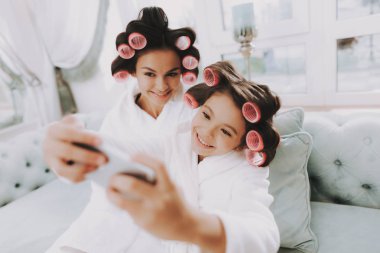 Curlers ile küçük hanım. Anne ve kızı Spa. Consept güzellik salonu. Anne ve kız gülümsüyor. Güzel yüzüm. Kadın ve mutlu bir çocuk. Curlers kadınla. Selfie yapıyor. Spa salonda mavi kanepe.